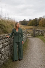 Euphrasie green tie waist jacket and trouser set beside an autumn stone wall