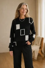 Grace black geometric knit sweater with white square motifs, worn by the main product model with one hand in her trouser pocket
