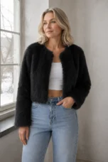 Idola black cropped faux-fur jacket on the main product model, with one hand in her jeans pocket beside a window