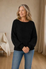Jane black rib-knit sweater on the main product model, hands loosely joined and looking to the side