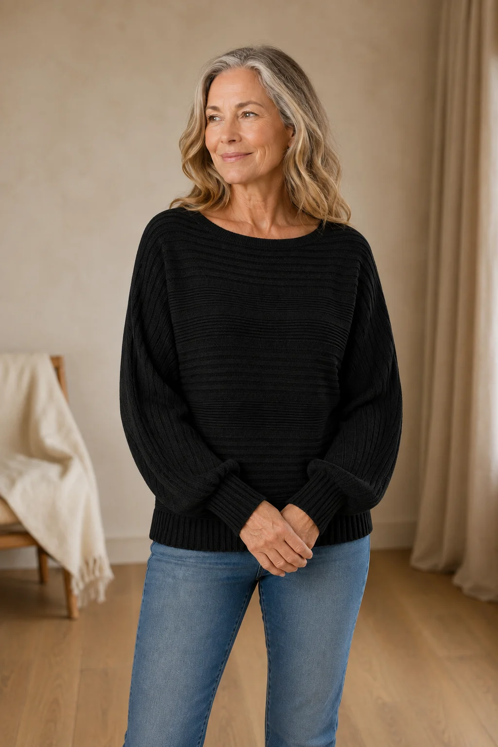 Jane black rib-knit sweater on the main product model, hands loosely joined and looking to the side