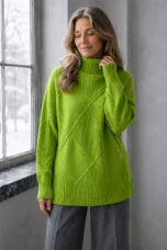 Kathleen green textured turtleneck sweater, model with long wavy hair gently touching the collar and looking down beside a window.
