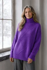 Kathleen purple textured turtleneck sweater, model with long wavy hair leaning gently against a wall beside a window.