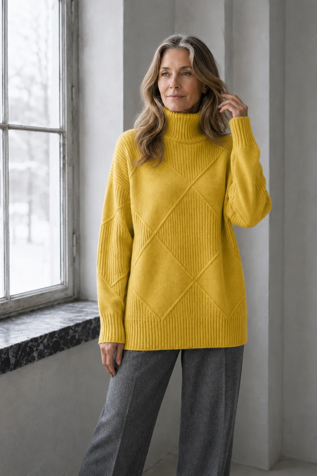 Kathleen yellow textured turtleneck sweater, model with long wavy hair gently touching a strand beside a window.